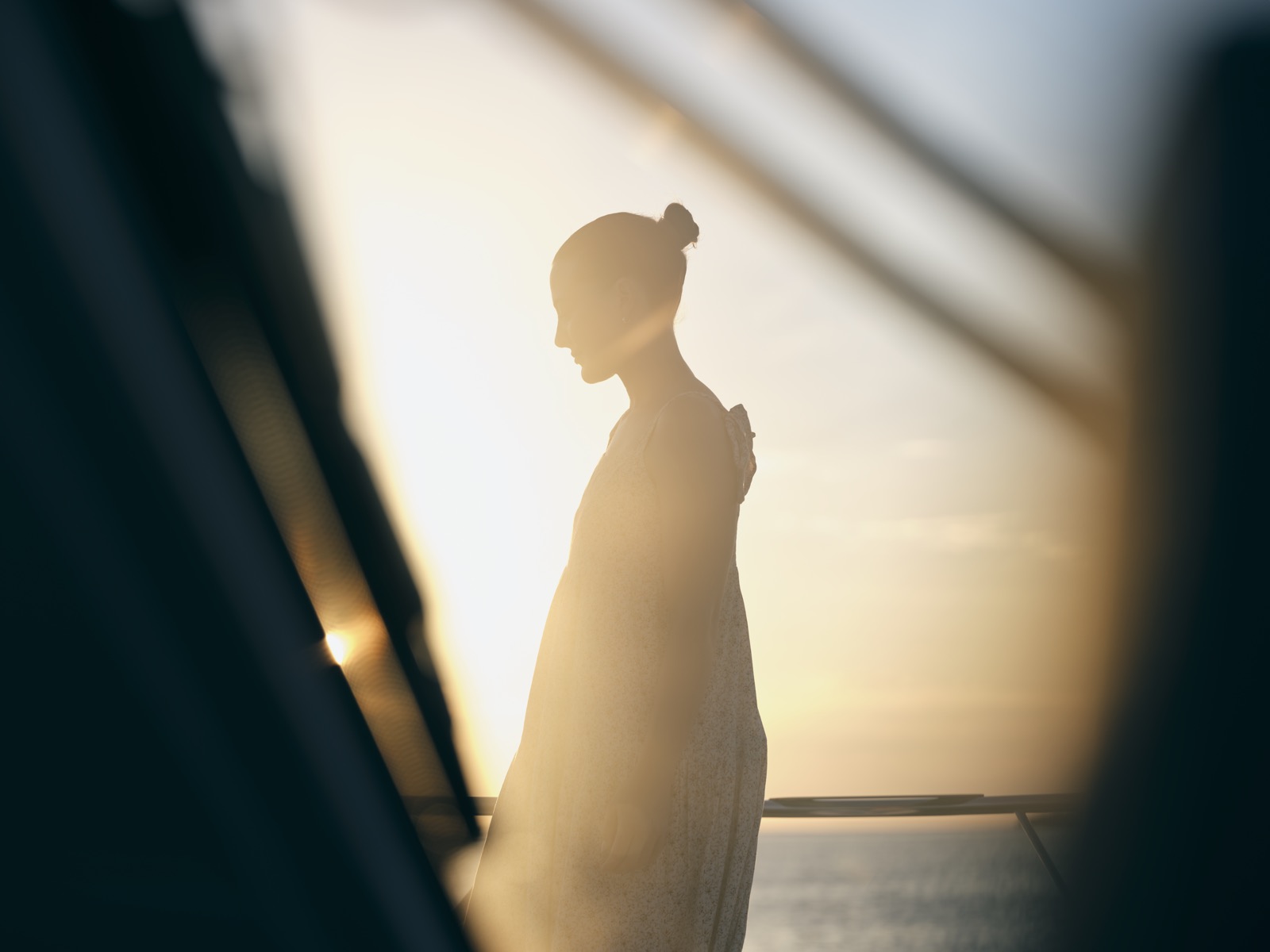 Silhouette d’une femme à bord d’un navire face à la mer, au coucher du soleil.