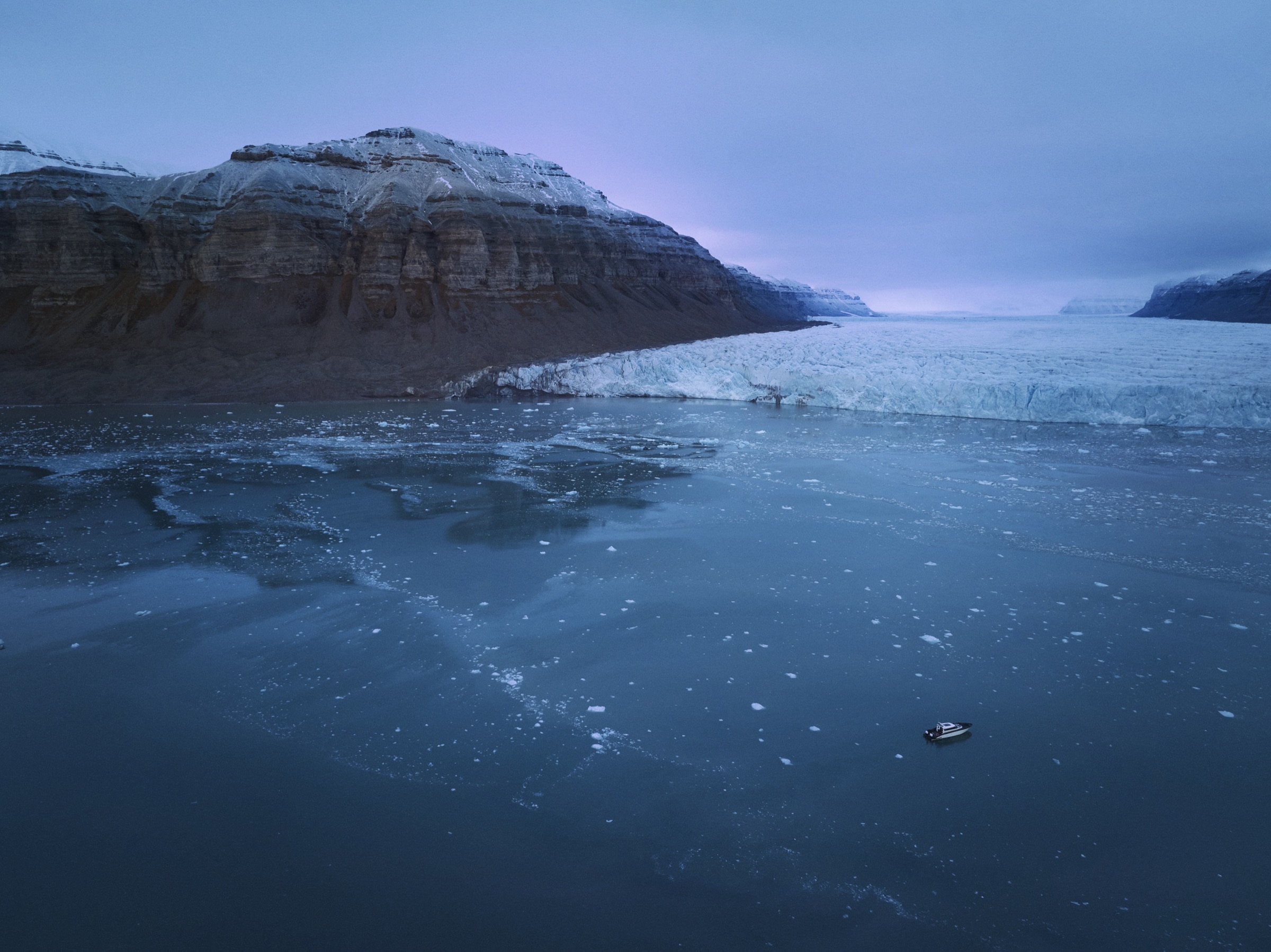 Vue aérienne d’un navire électrique naviguant en eaux froides, au pied d’un glacier et de falaises côtières.